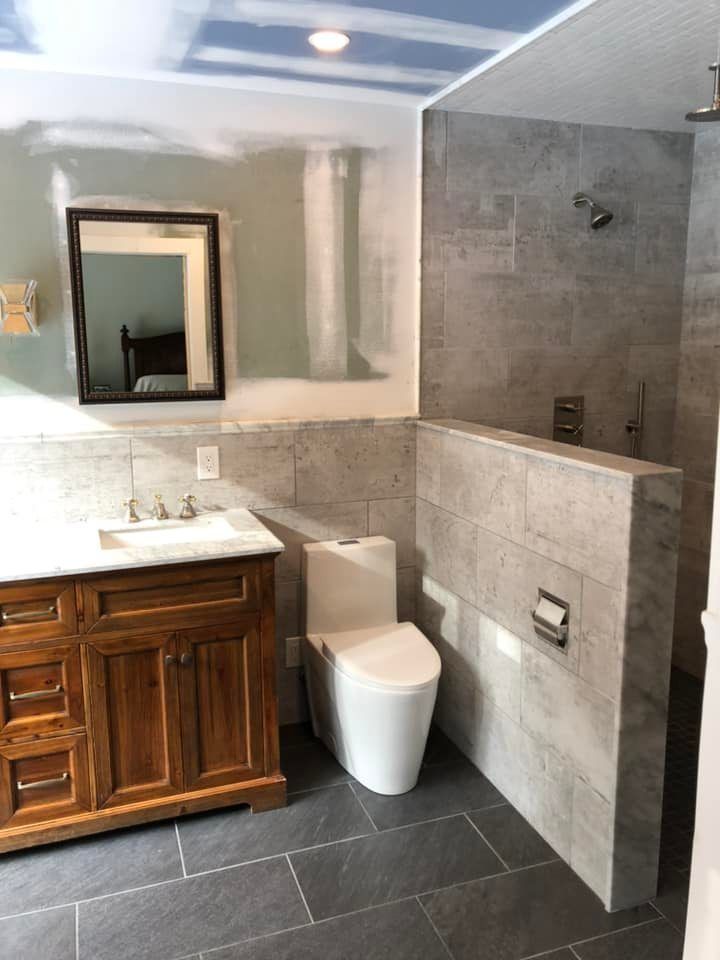 Bathroom under renovation with gray tiled shower and walls, dark wood vanity, white toilet.