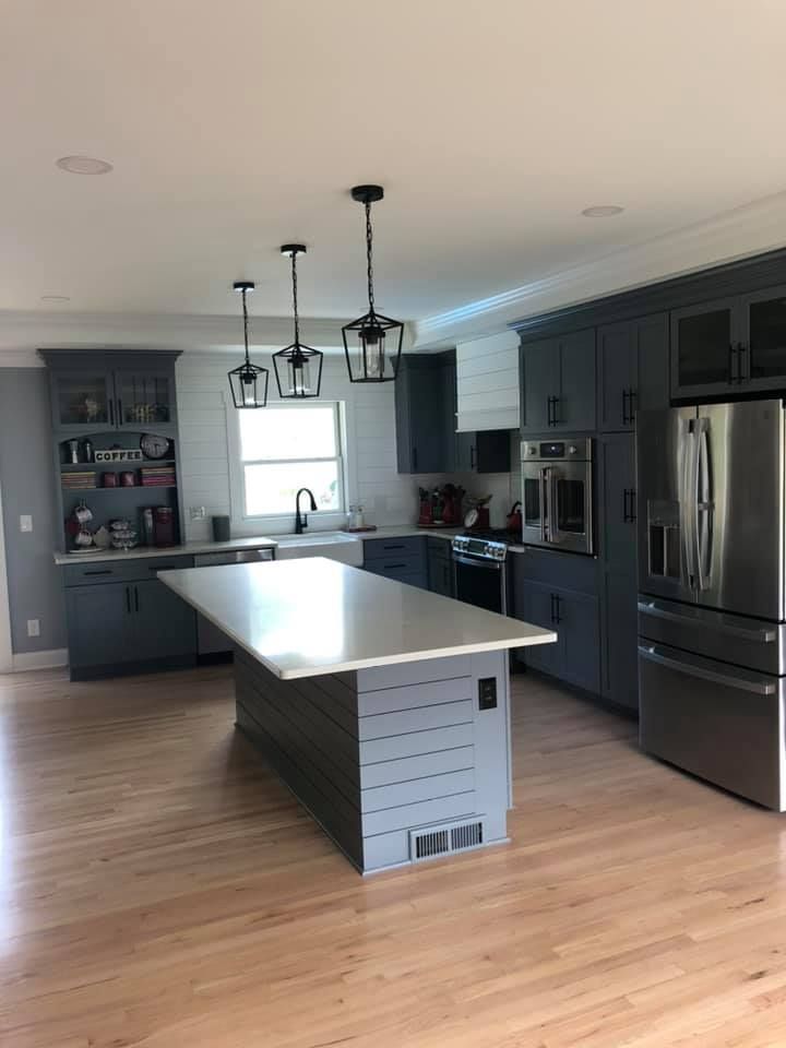 Modern kitchen with gray cabinets, white countertops, wooden floors, and a kitchen island with pendant lights.