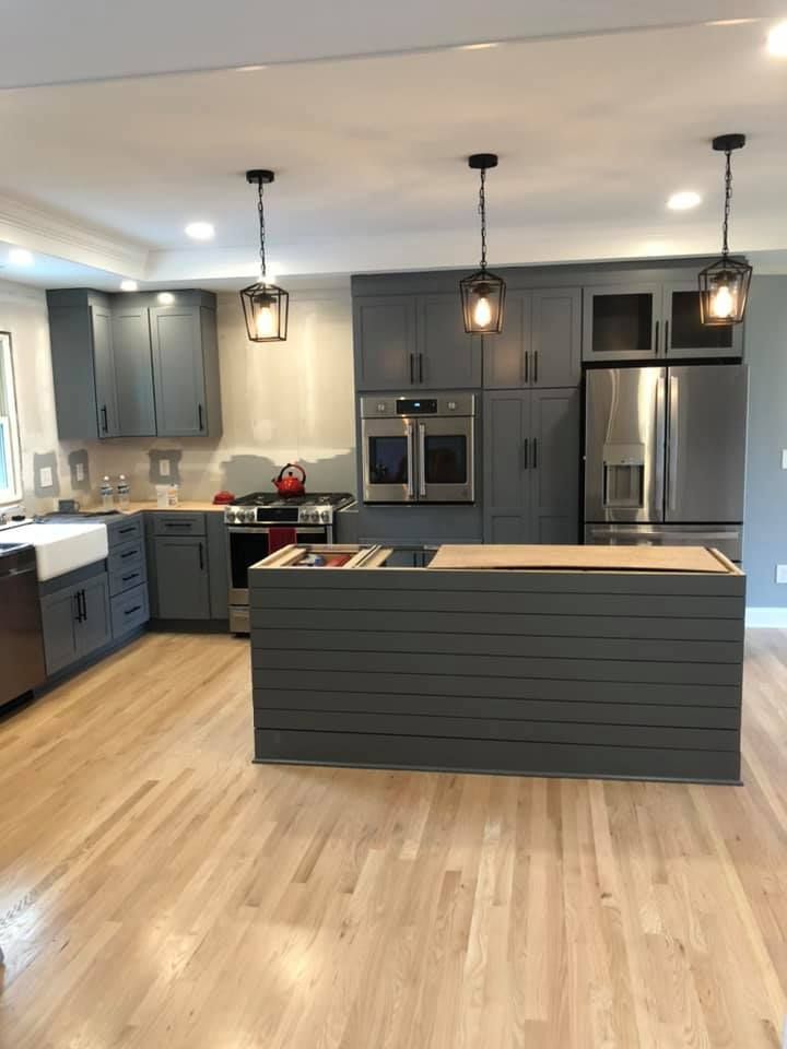Gray kitchen with light wood floors, gray cabinets, stainless steel appliances, and island with hanging lights.