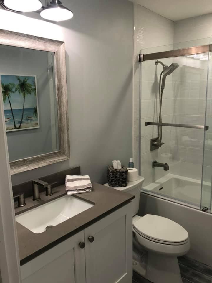 Bathroom with a vanity, toilet, and shower/tub. Blue walls, a framed mirror, and a beach painting.