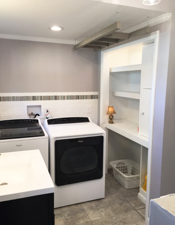 Laundry room with a washer, dryer, built-in shelves, and a folding table. White and gray tones.