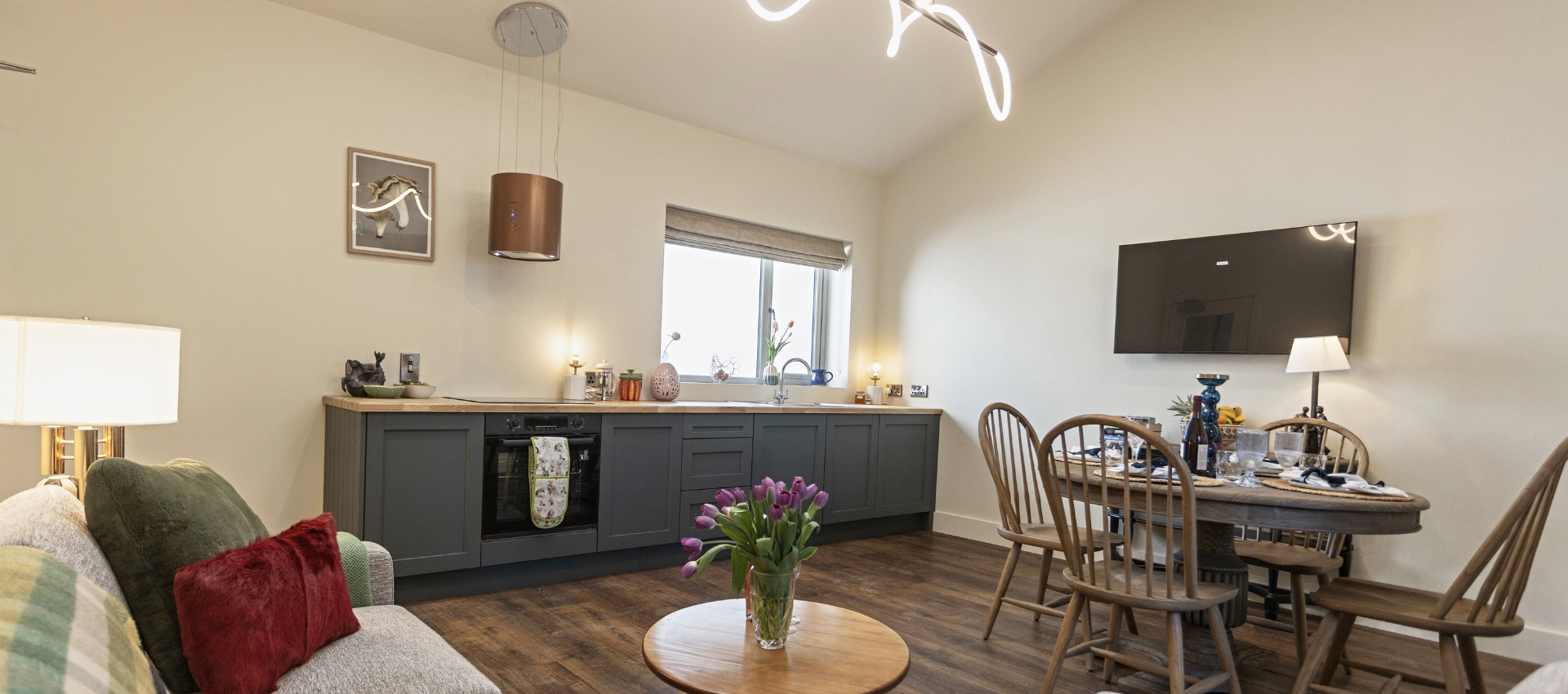 Cozy dining and living room with gray sideboard, round table, wall art, and sofa by the window.