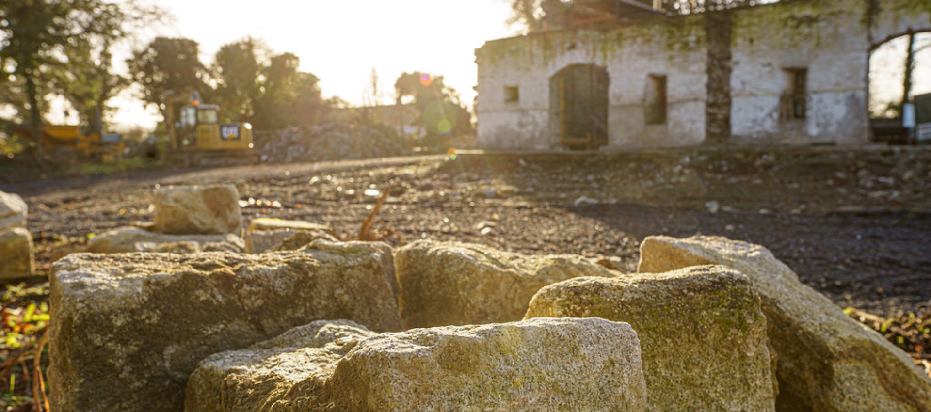Sunlit ancient stone ruins in a grassy field with a small white building in the background