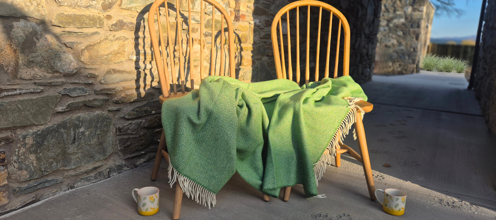 A wooden chair with a green blanket and two cups on it.