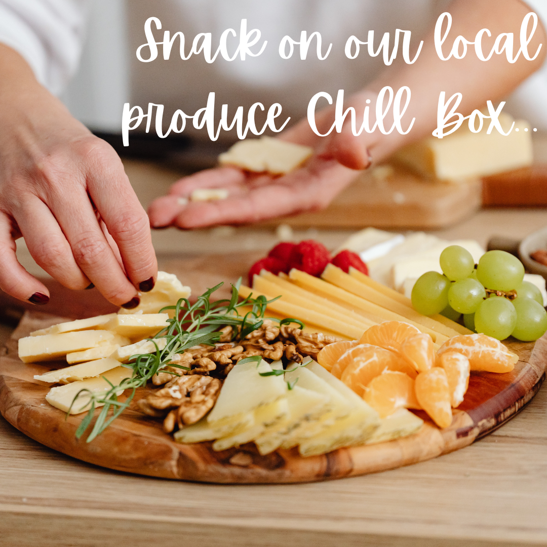 A person is taking a piece of cheese from a cutting board that says snack on our local produce chill box