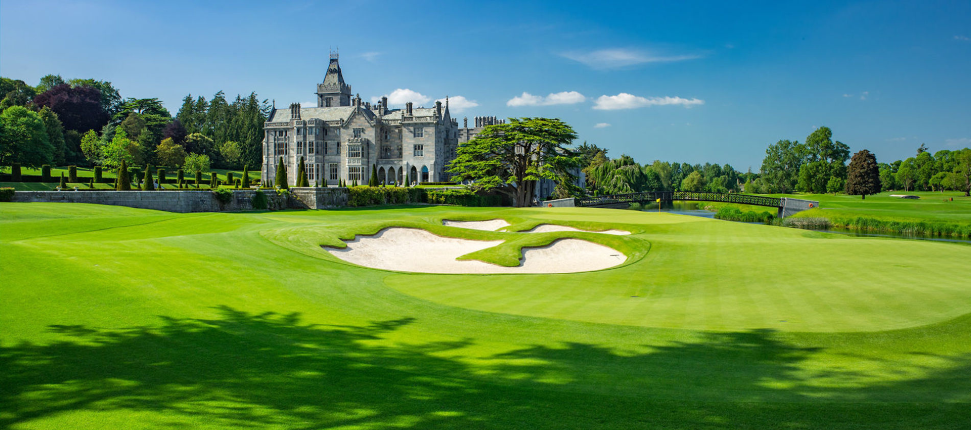Golf course with a sand bunker in front of a white castle-style clubhouse under a blue sky