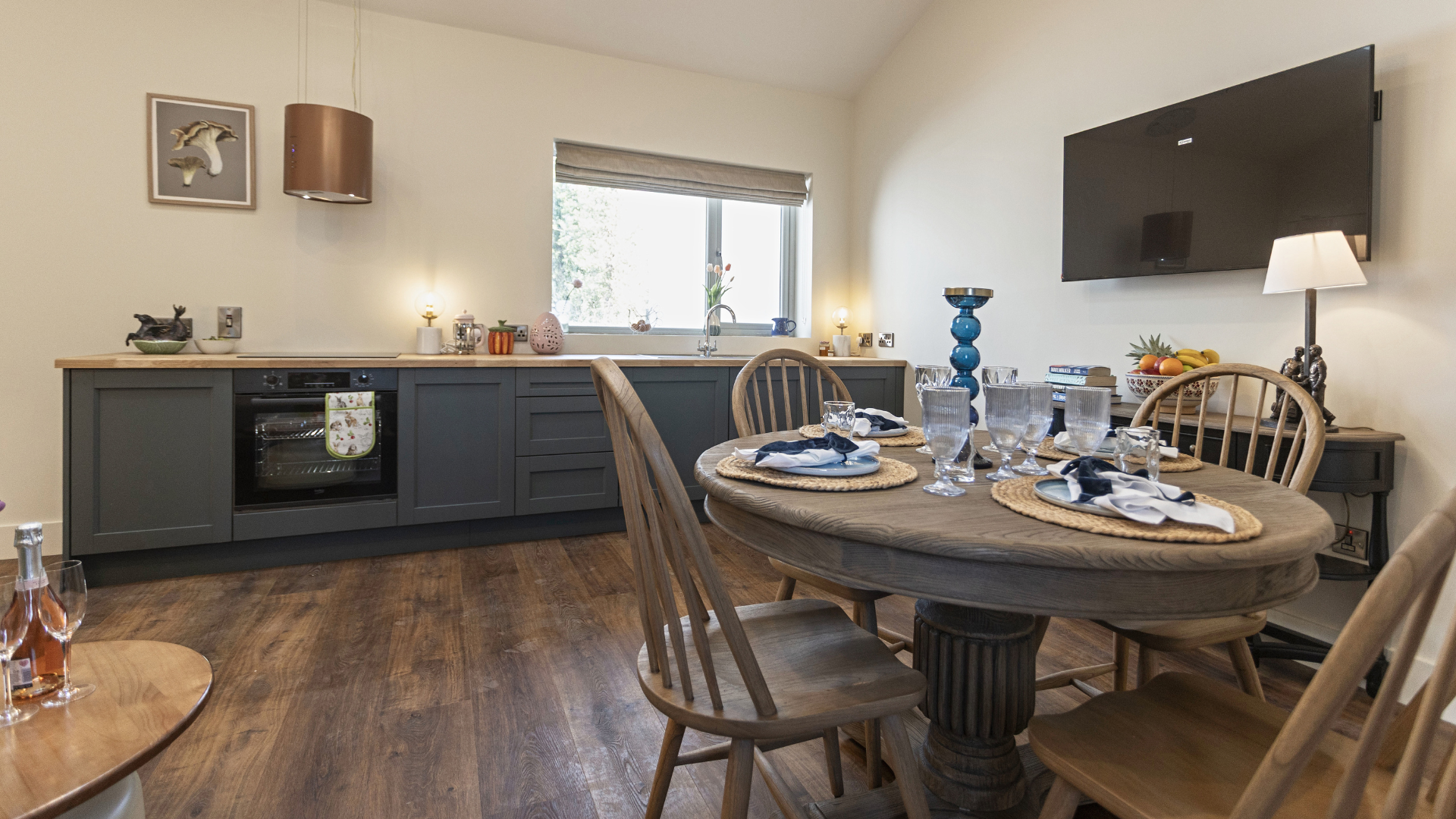 Dining room with set table, dark sideboard, wall-mounted TV, and window with chairs around wooden table