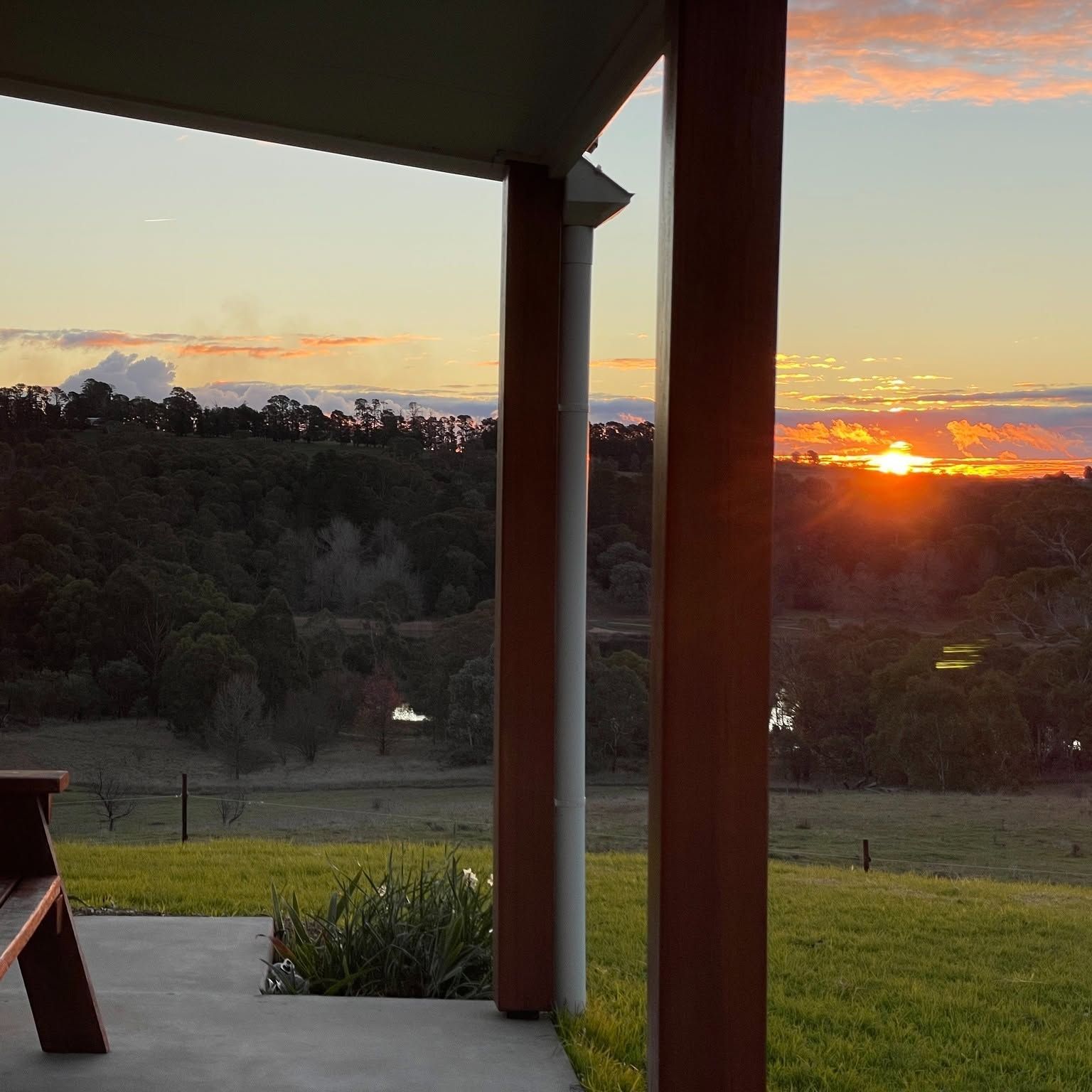 Sunset Over Grassy Hills Viewed From a Porch With Wooden Posts and a Bench — Lakeview Luxury Retreat in Canobolas, NSW