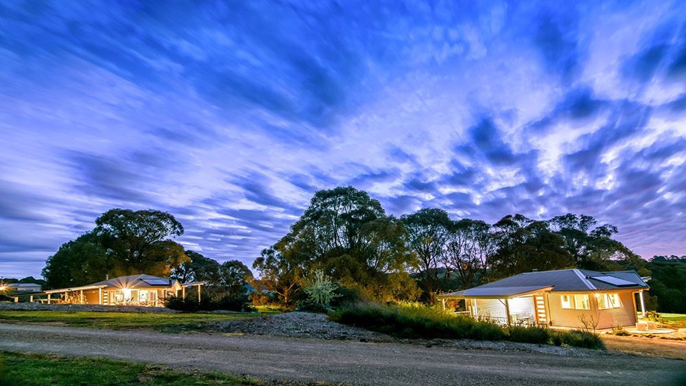 A Group of Houses Are Sitting on Top of a Dirt Field Under a Cloudy Sky — Lakeview Luxury Retreat in Canobolas, NSW