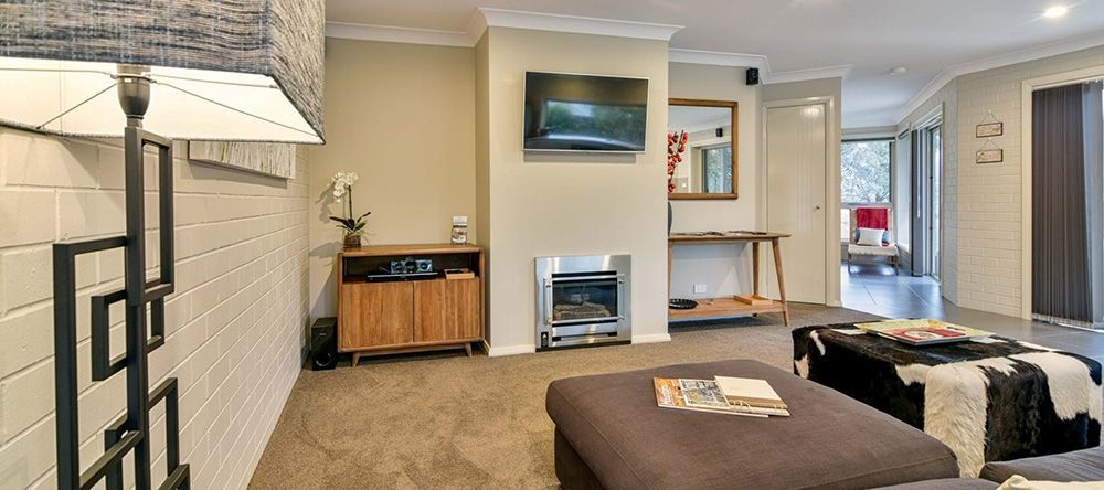 A Living Room With a Couch, Ottoman, Television and Fireplace — Lakeview Luxury Retreat in Canobolas, NSW