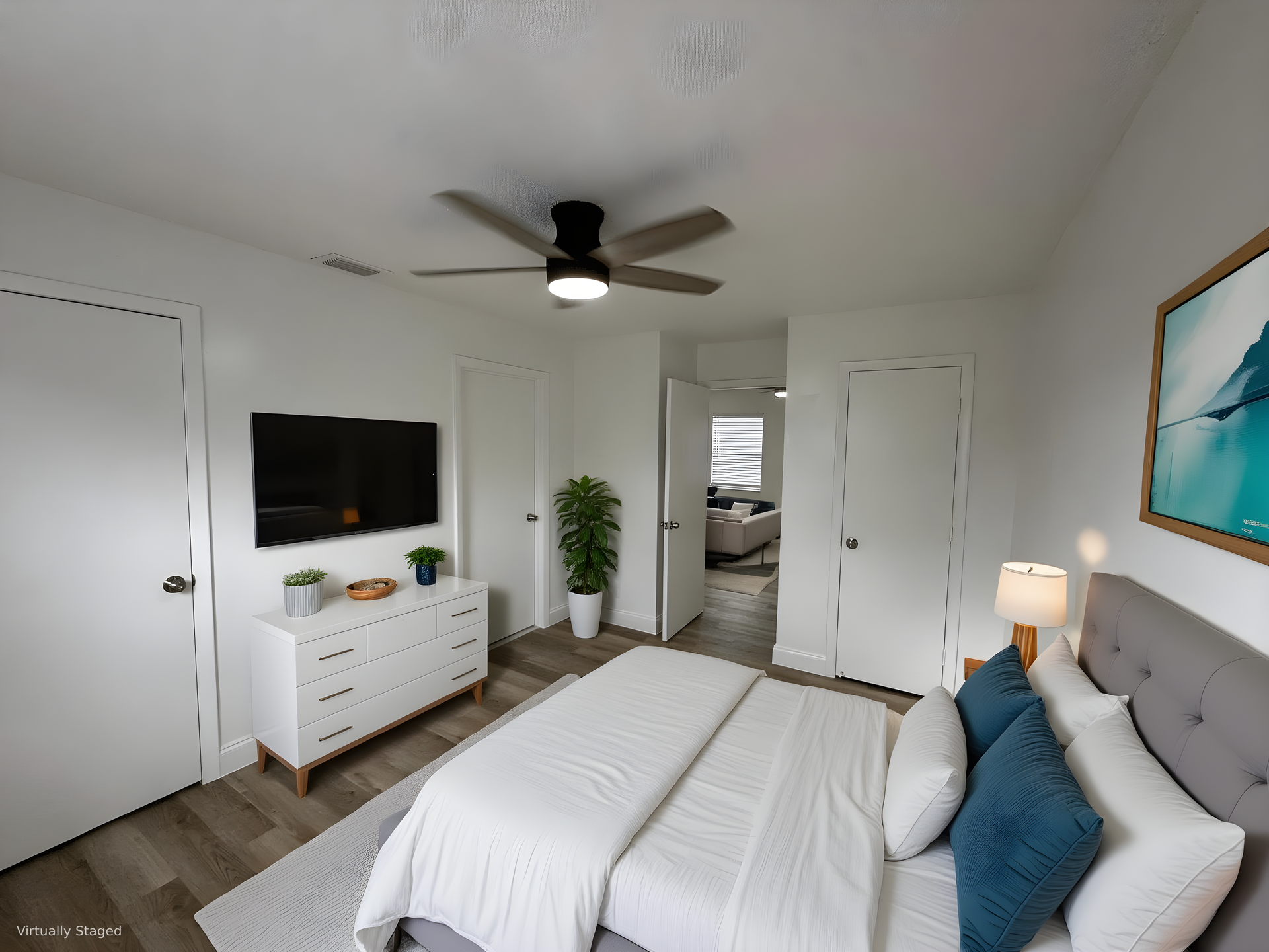 Bedroom with bed, dresser, TV, and ceiling fan; a door leads to another room.