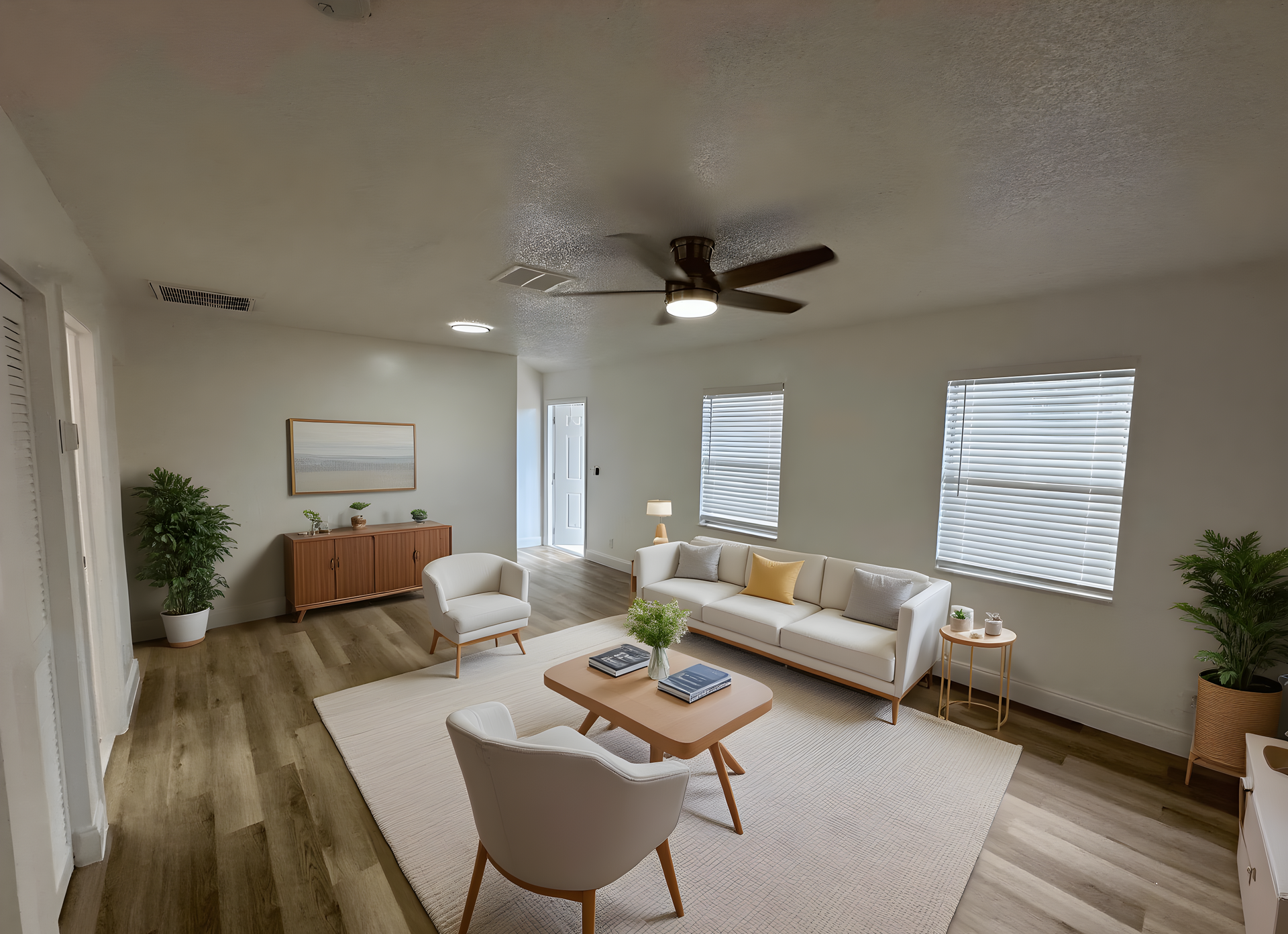 Living room with white walls, tan wood floors, light furniture, and area rug.