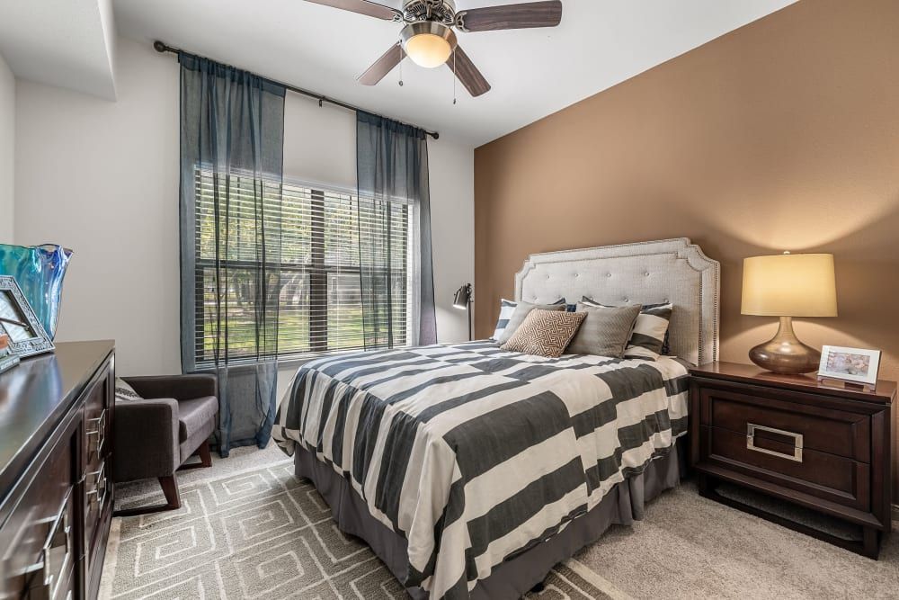 a bedroom with a bed, nightstand, chair, and ceiling fan at Marquis on Lakeline in Cedar Park, TX.