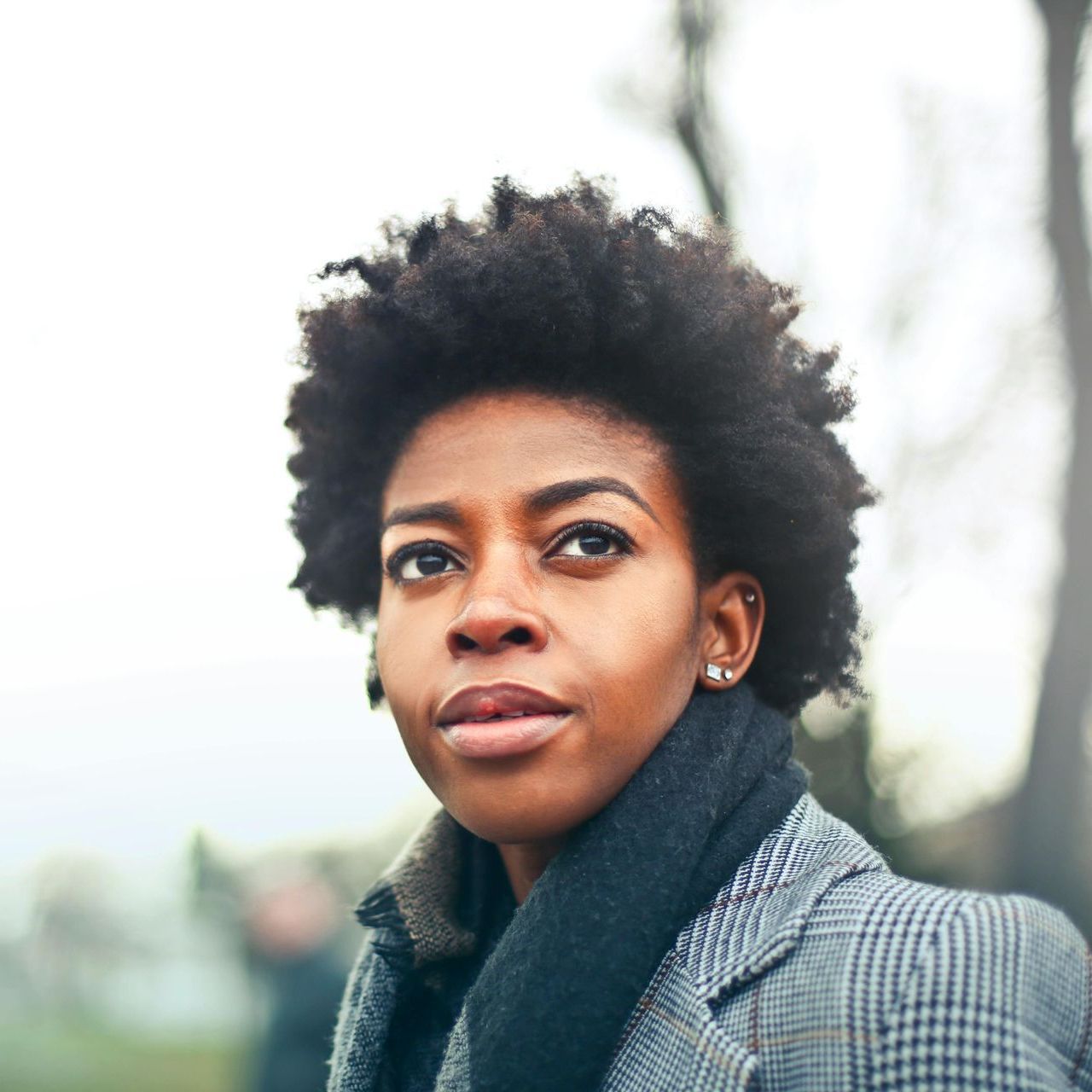 Woman with natural hair and a gray coat looks up, soft focus background.