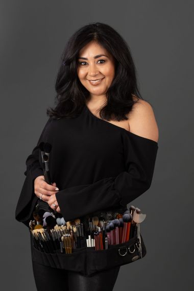 A woman in a black off the shoulder top is holding makeup brushes.