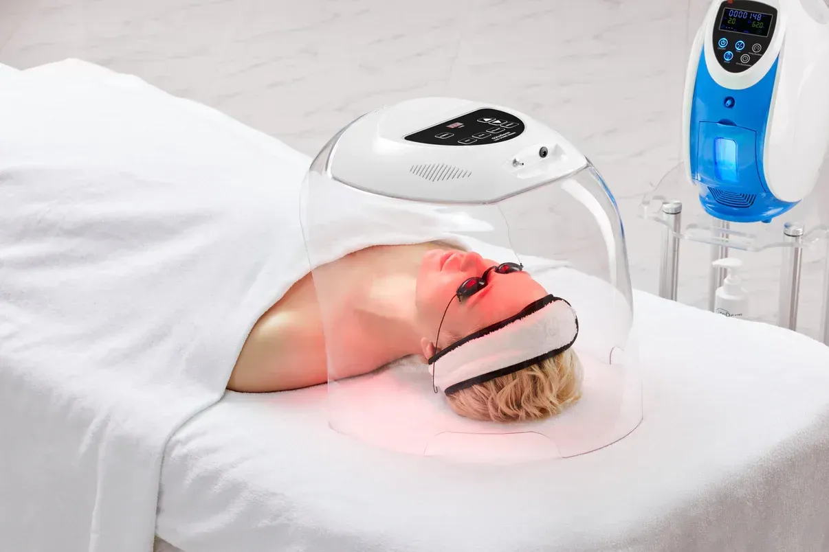 A woman is laying on a bed getting a treatment on her face.