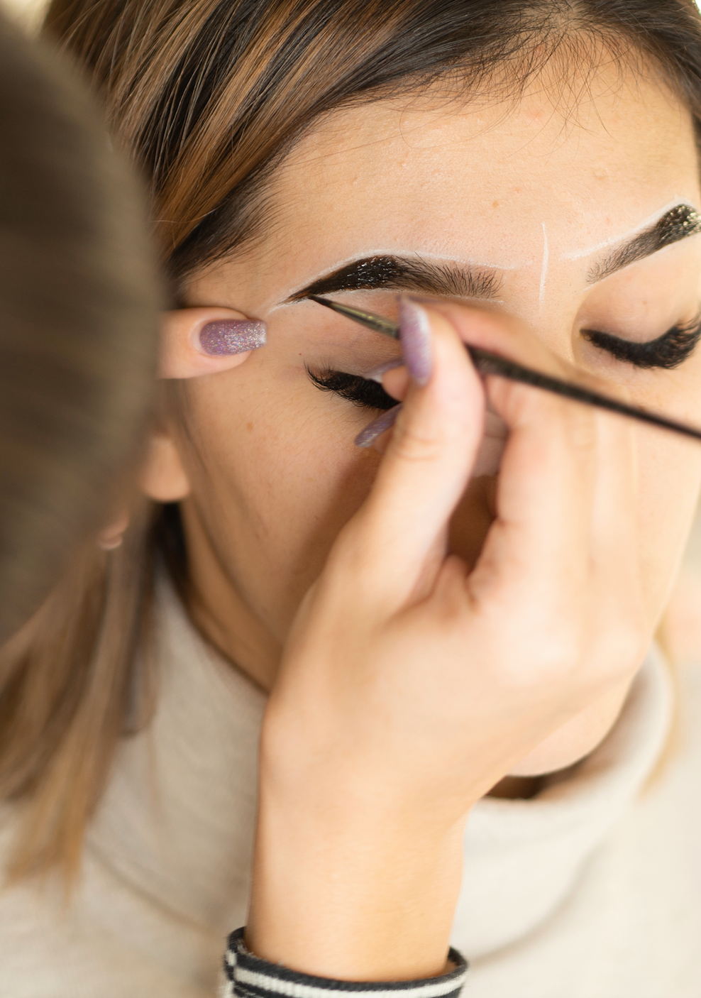 A woman is getting her eyebrows painted by a makeup artist.