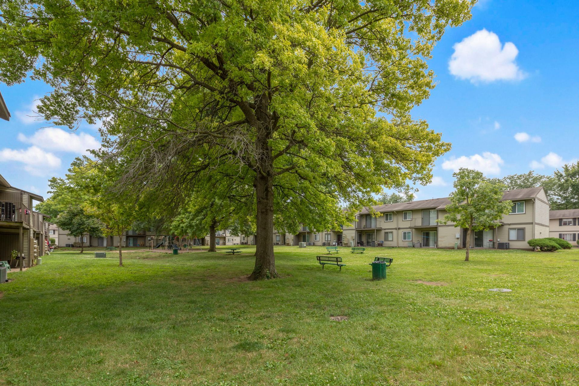 Green, grassy courtyard with trees, picnic tables, and two-story apartment buildings.