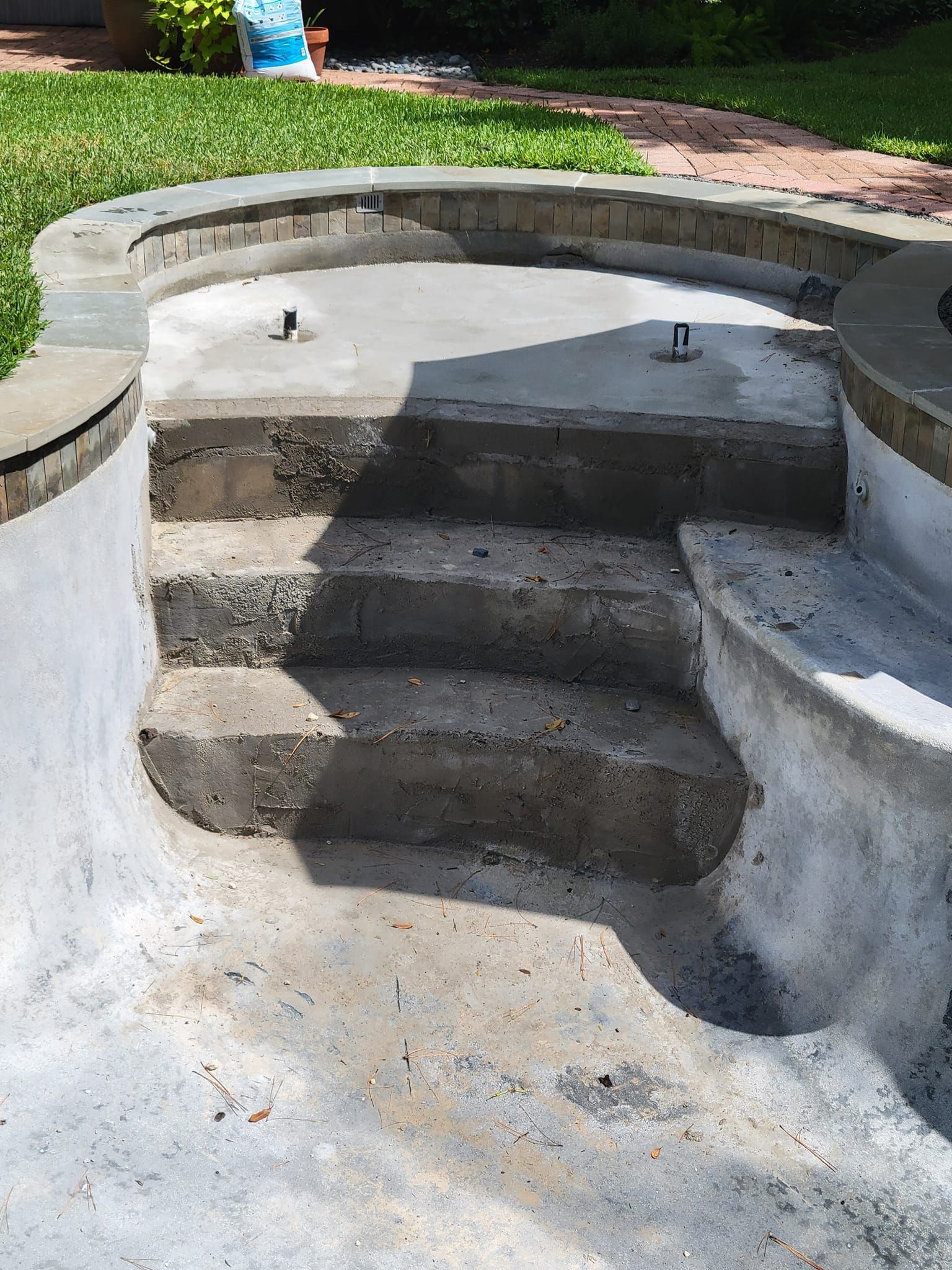 Concrete backyard steps leading into an empty in-ground pool shell with built-in seating