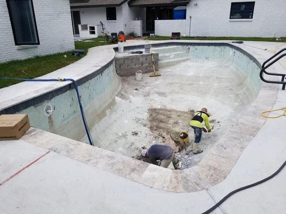 Workers repairing a drained backyard pool shell at a house, with tools and debris inside.