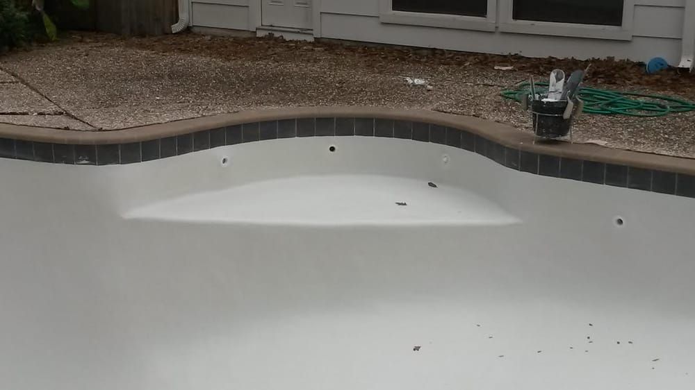 Empty white swimming pool beside a patio, with a person standing at the far edge.