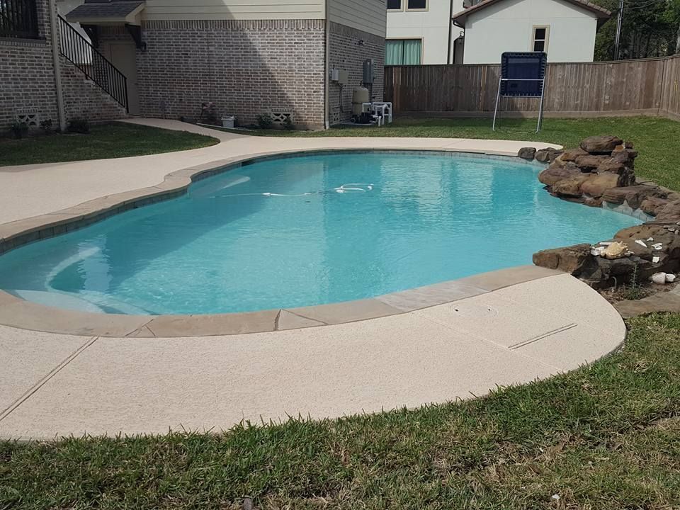 Backyard swimming pool with curved concrete deck and rock waterfall feature