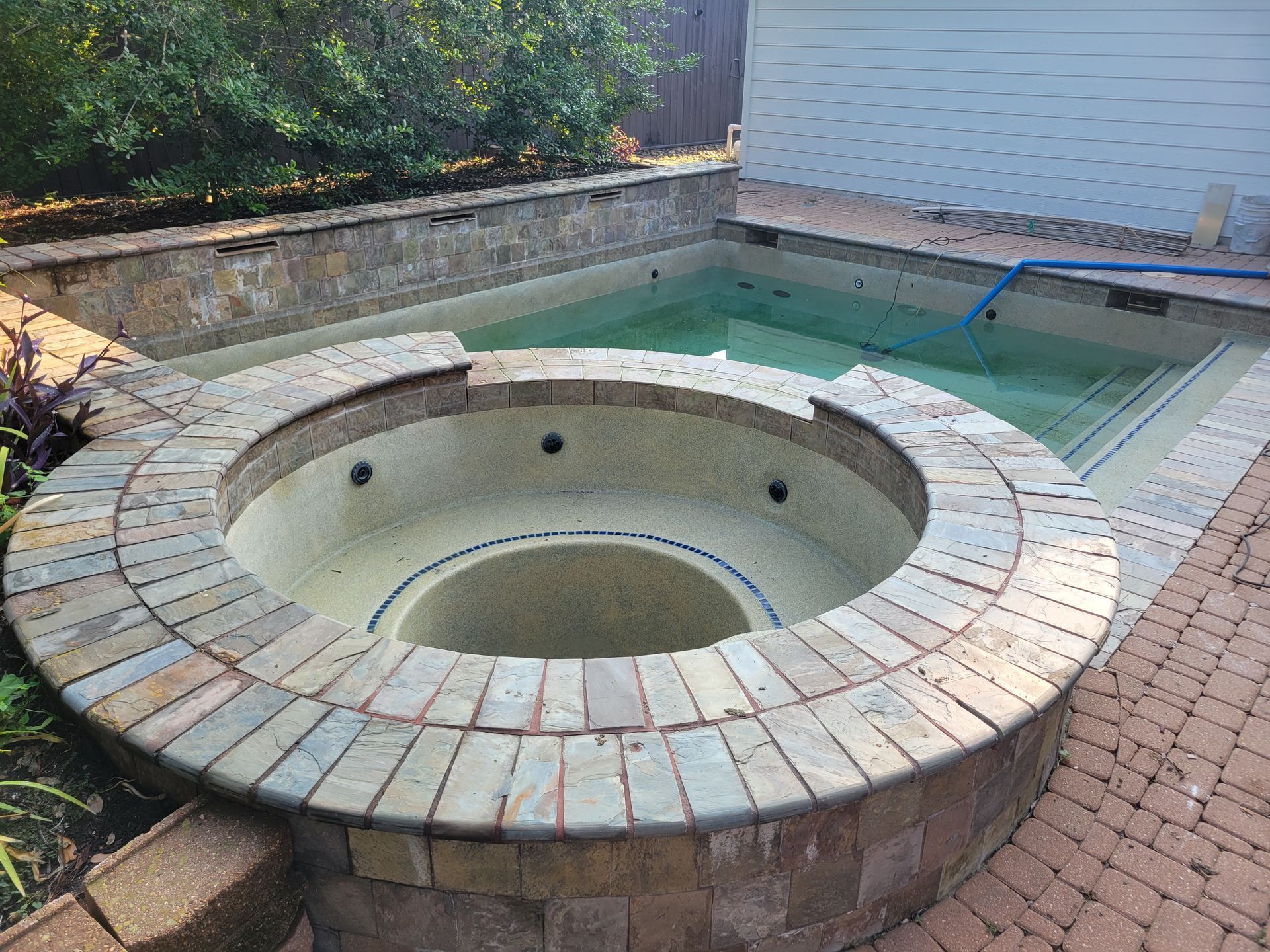 Empty circular hot tub in a backyard patio, with brick surround and built-in pool steps nearby