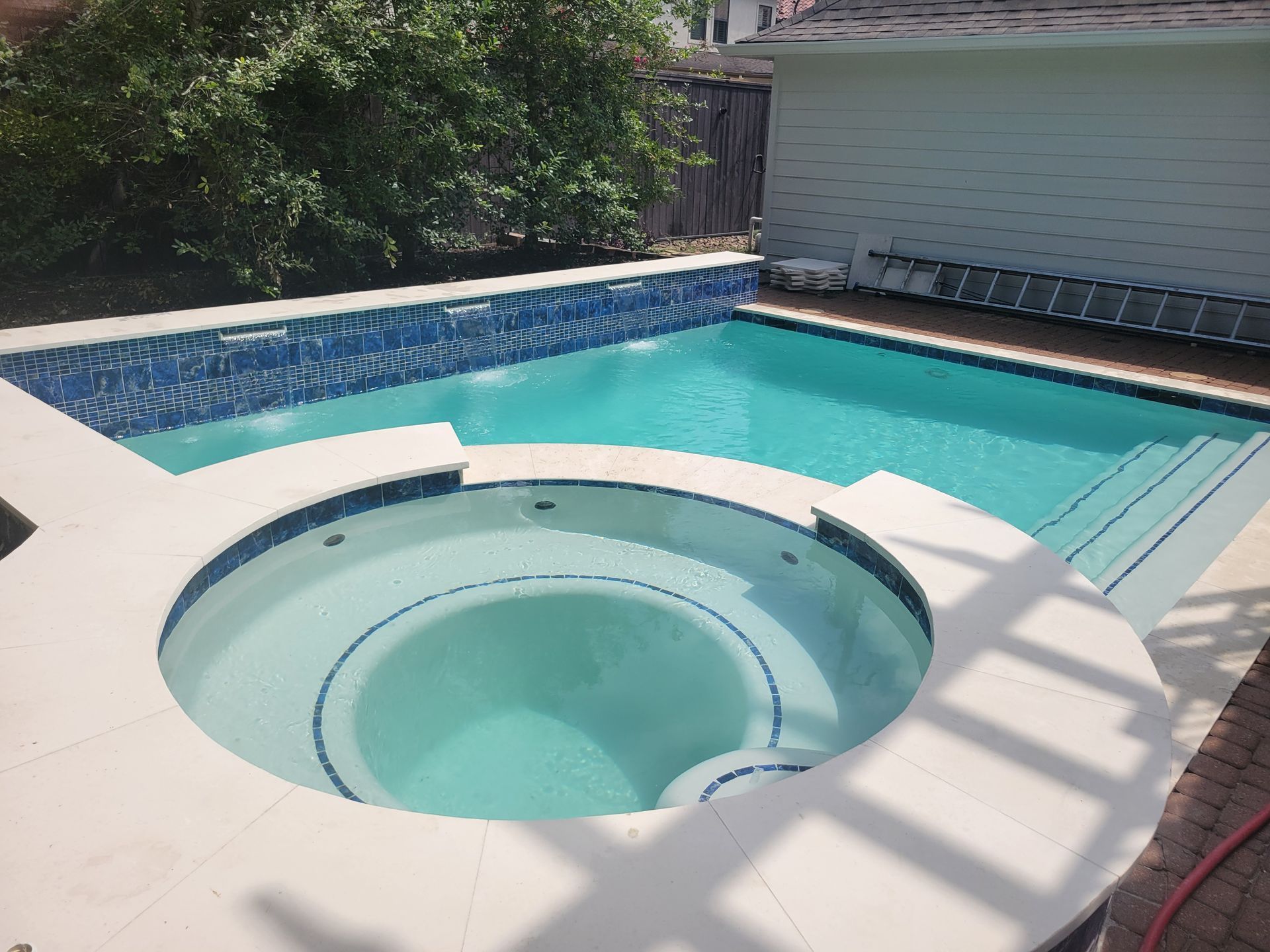 Backyard pool with a circular hot tub, turquoise water, and blue tile surround in sunlight