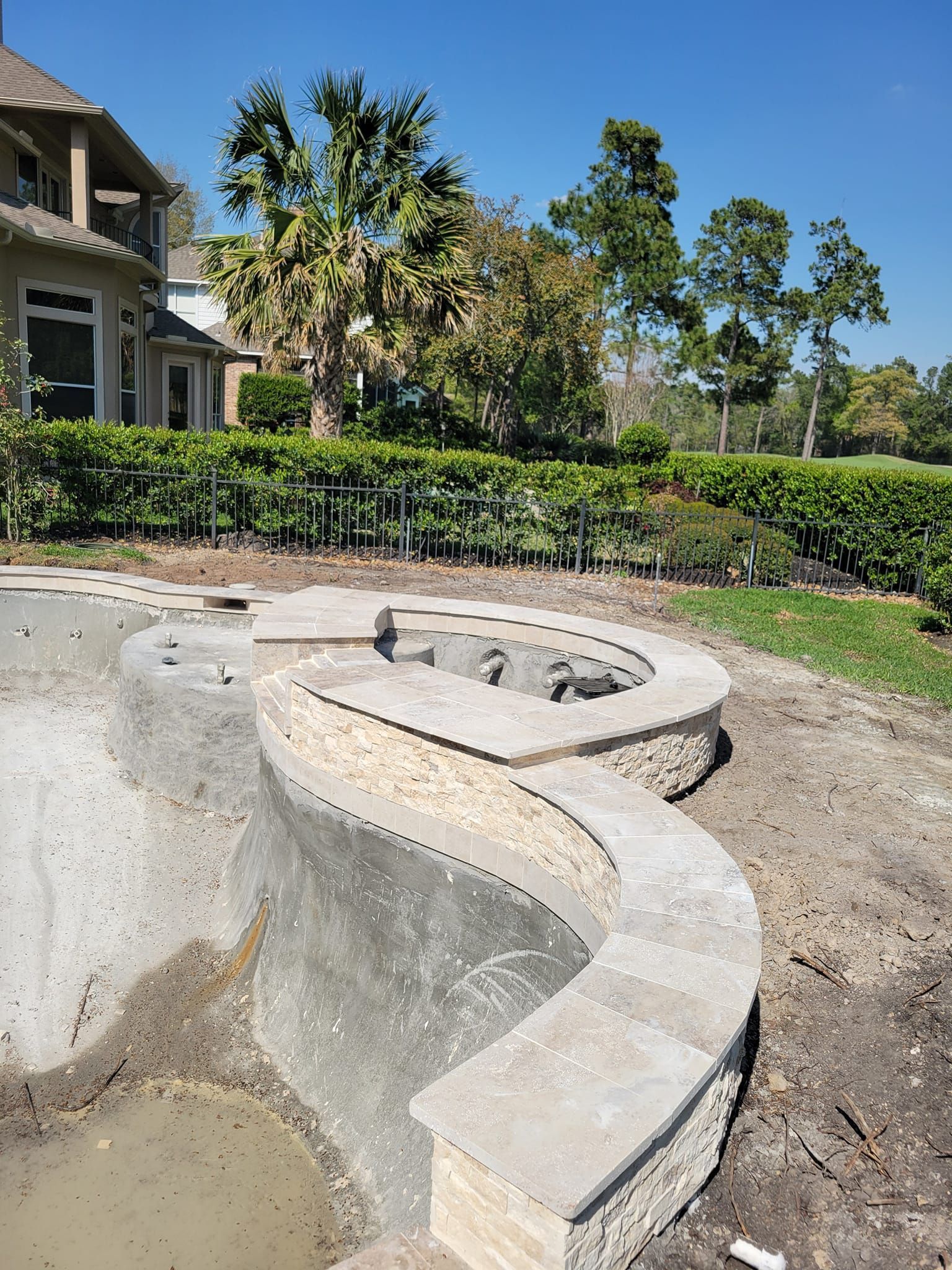 Curved concrete fire pit in a landscaped yard beside a house with hedges and palm trees