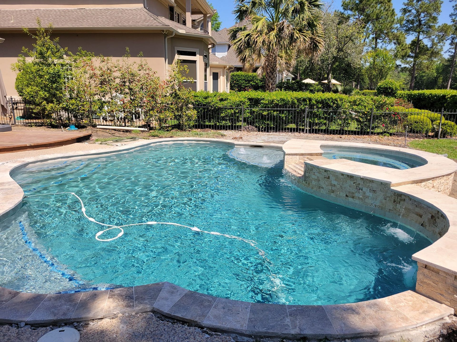 Backyard swimming pool with blue water, stone spa, and landscaped patio beside a house