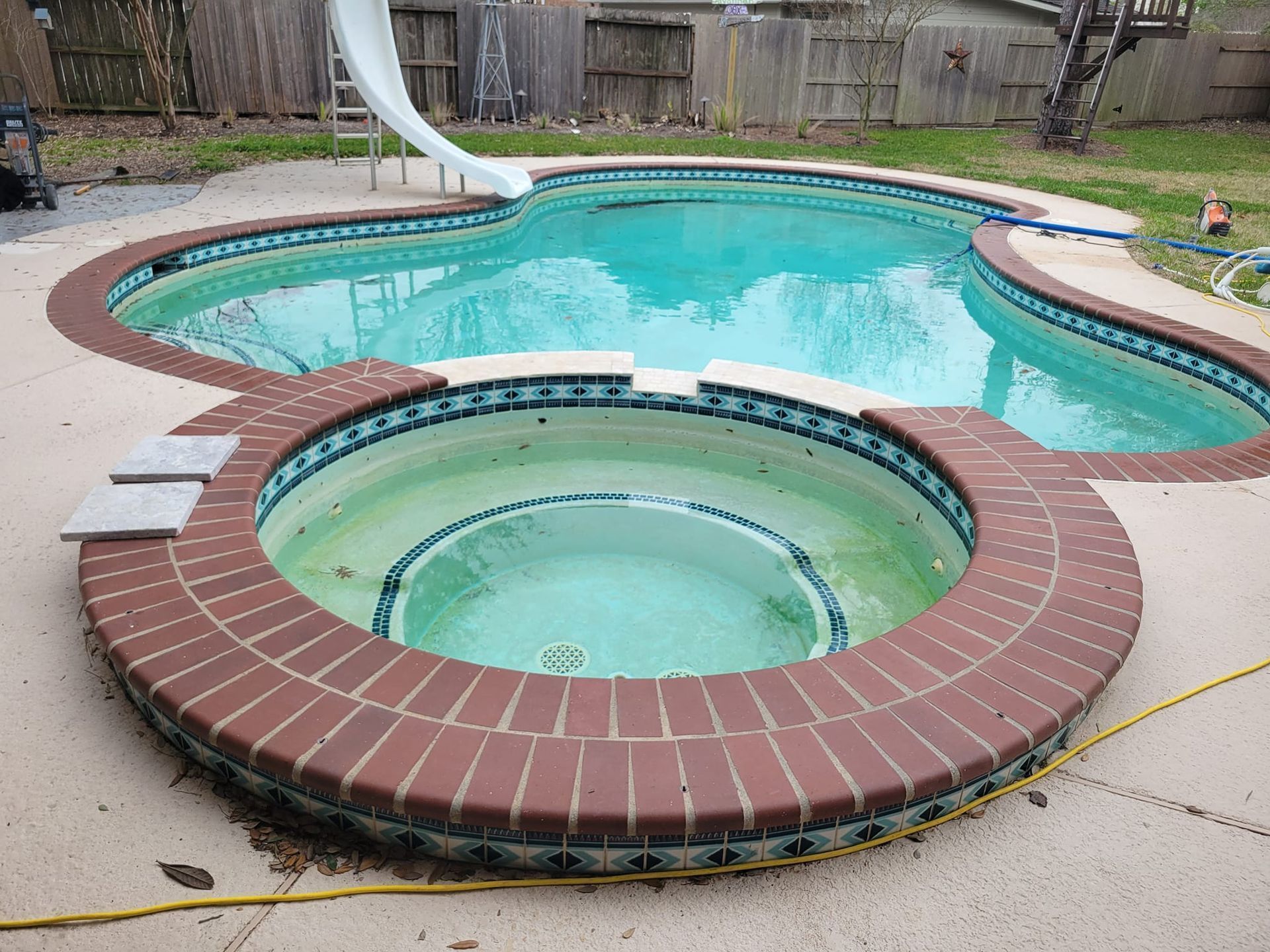 Backyard swimming pool with attached circular hot tub, brick coping, and a slide
