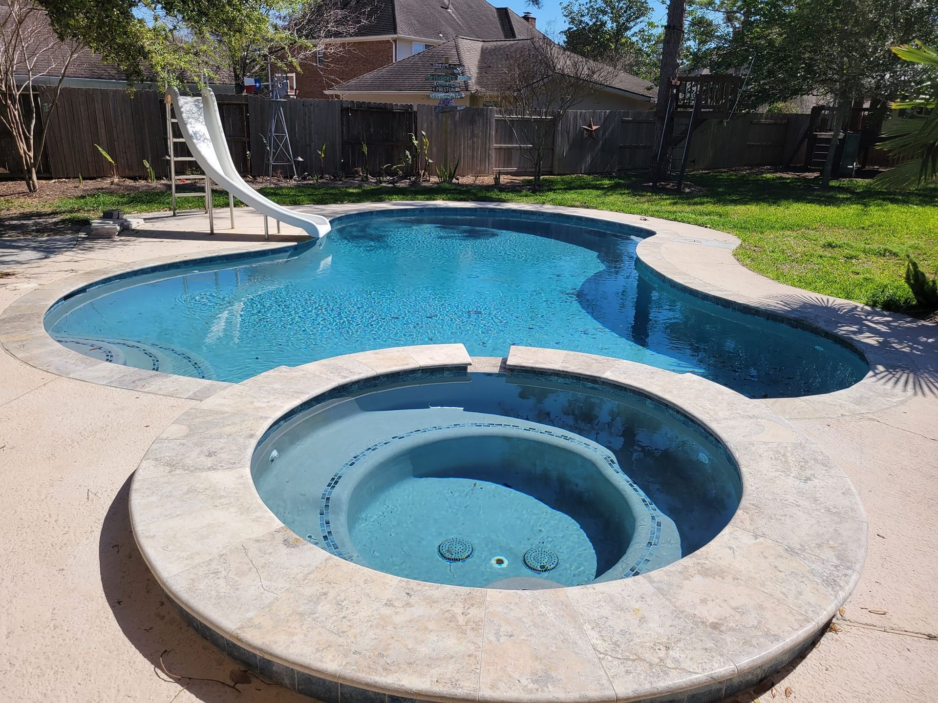 Backyard swimming pool with attached hot tub and a white slide in a sunny yard