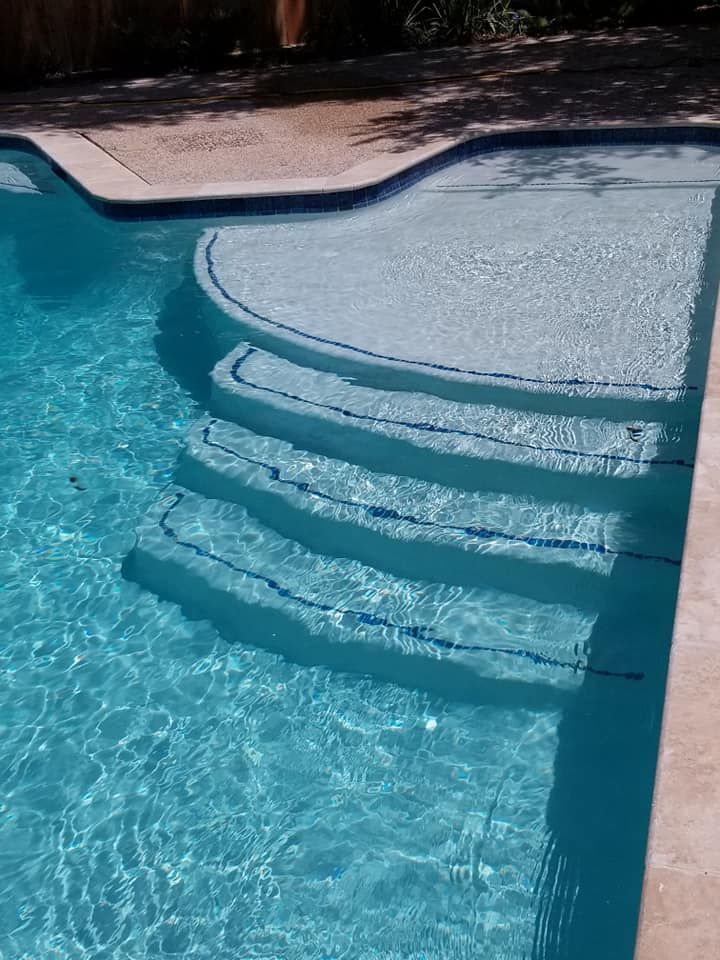 Curved swimming pool steps with a shallow sun shelf beside blue water and tan pool deck