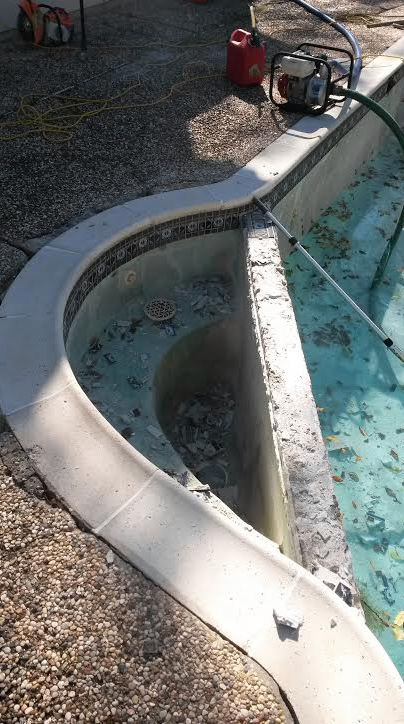 Small empty pool with white coping and blue interior beside a gravel patio and power equipment.