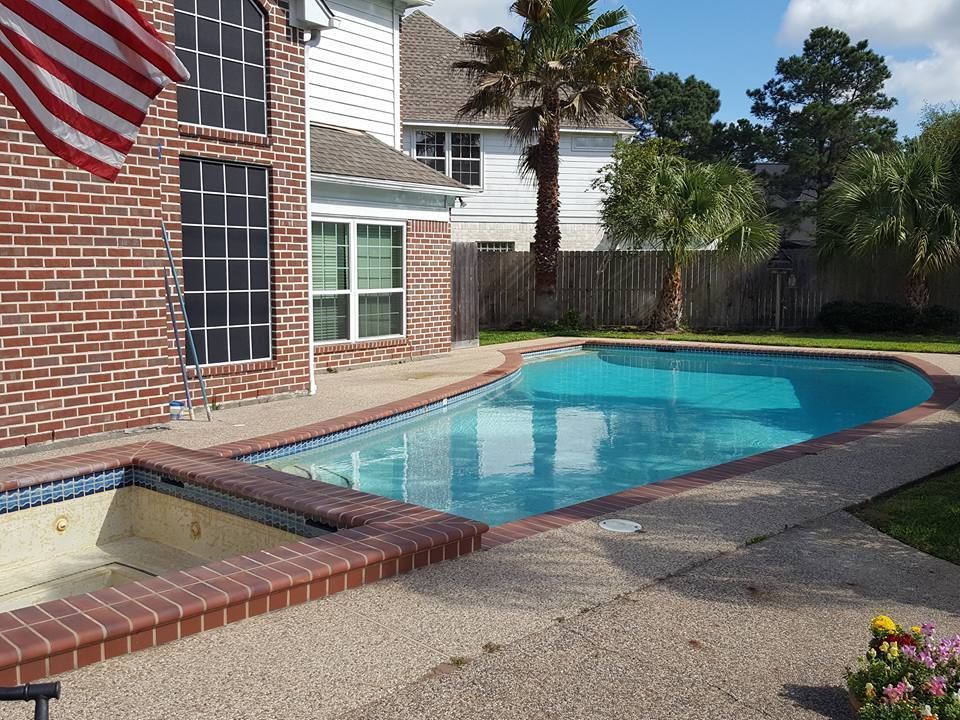 Backyard swimming pool beside a brick house, with an attached hot tub and palm trees.