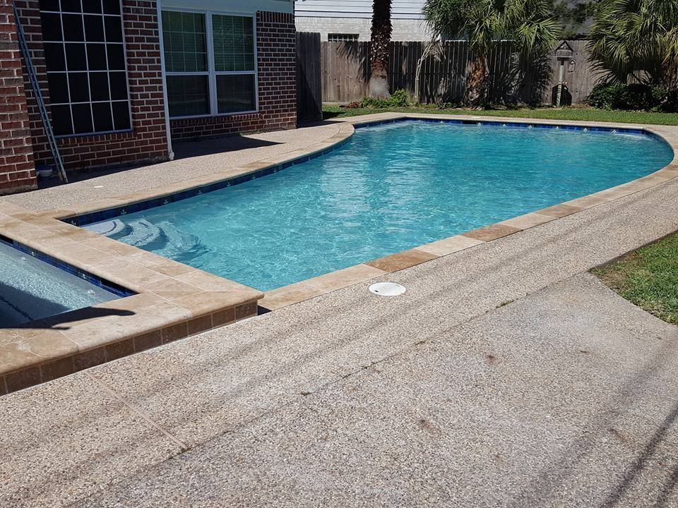 Backyard swimming pool with blue water beside a brick house and concrete patio