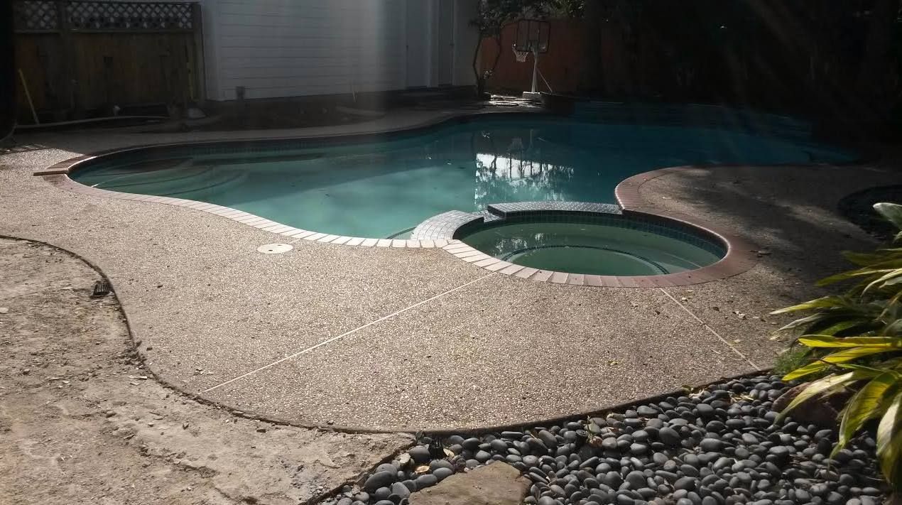 Backyard swimming pool with a raised spa, curved stone deck, and sunlight reflecting on the water