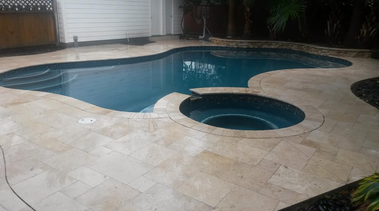 Backyard swimming pool with a raised circular spa and beige stone patio around it