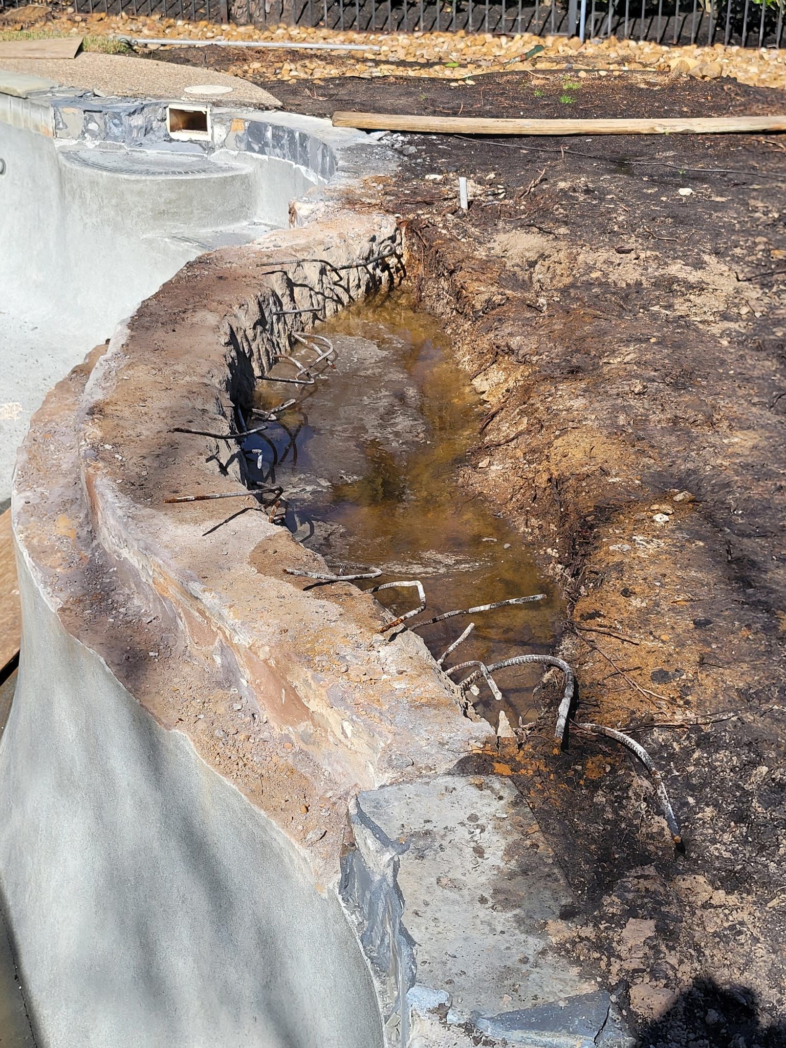 Damaged concrete curb with pooled water and scorched soil along a roadside edge
