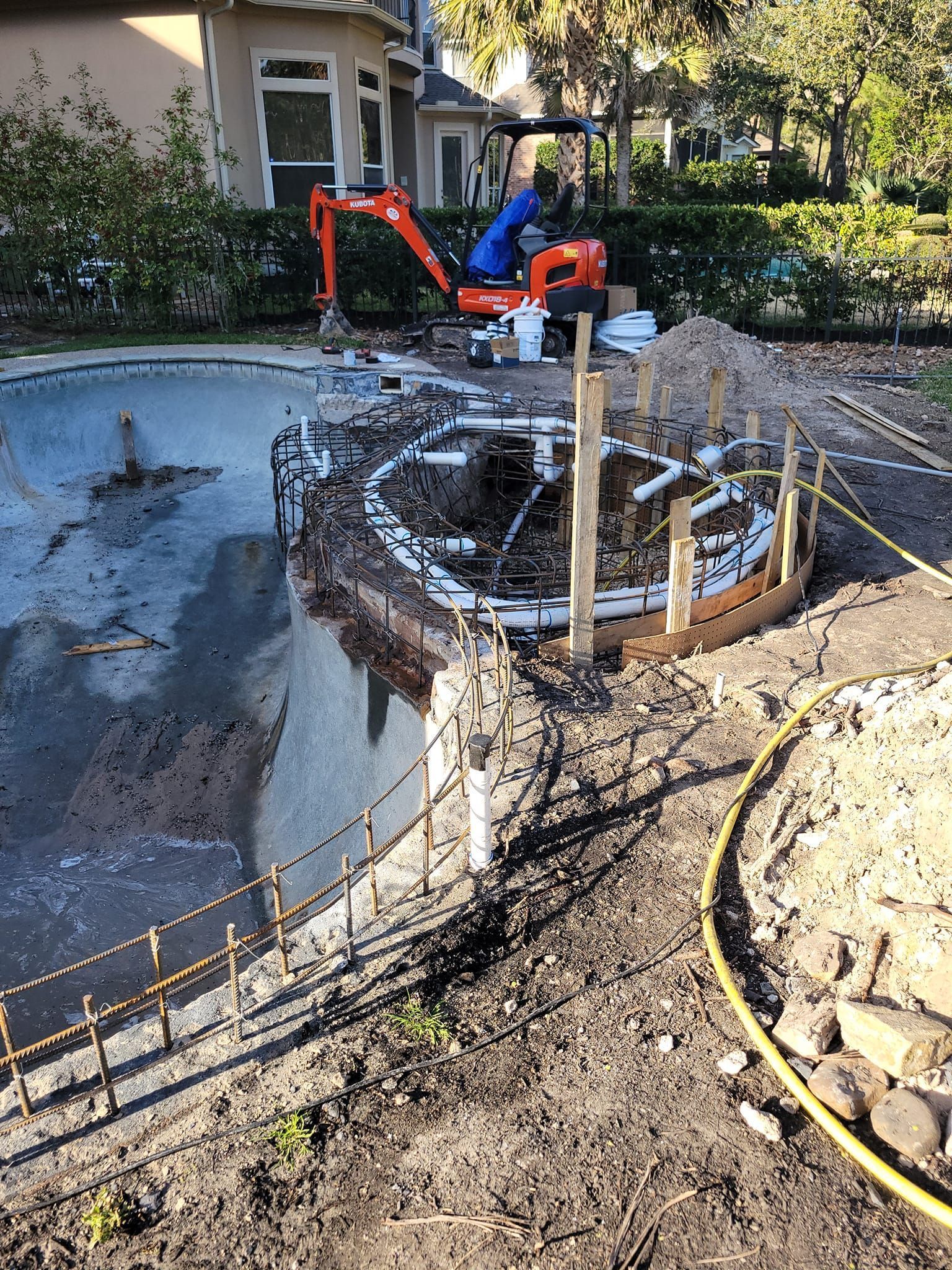 Worker using an orange excavator near a circular concrete pool under construction in a yard