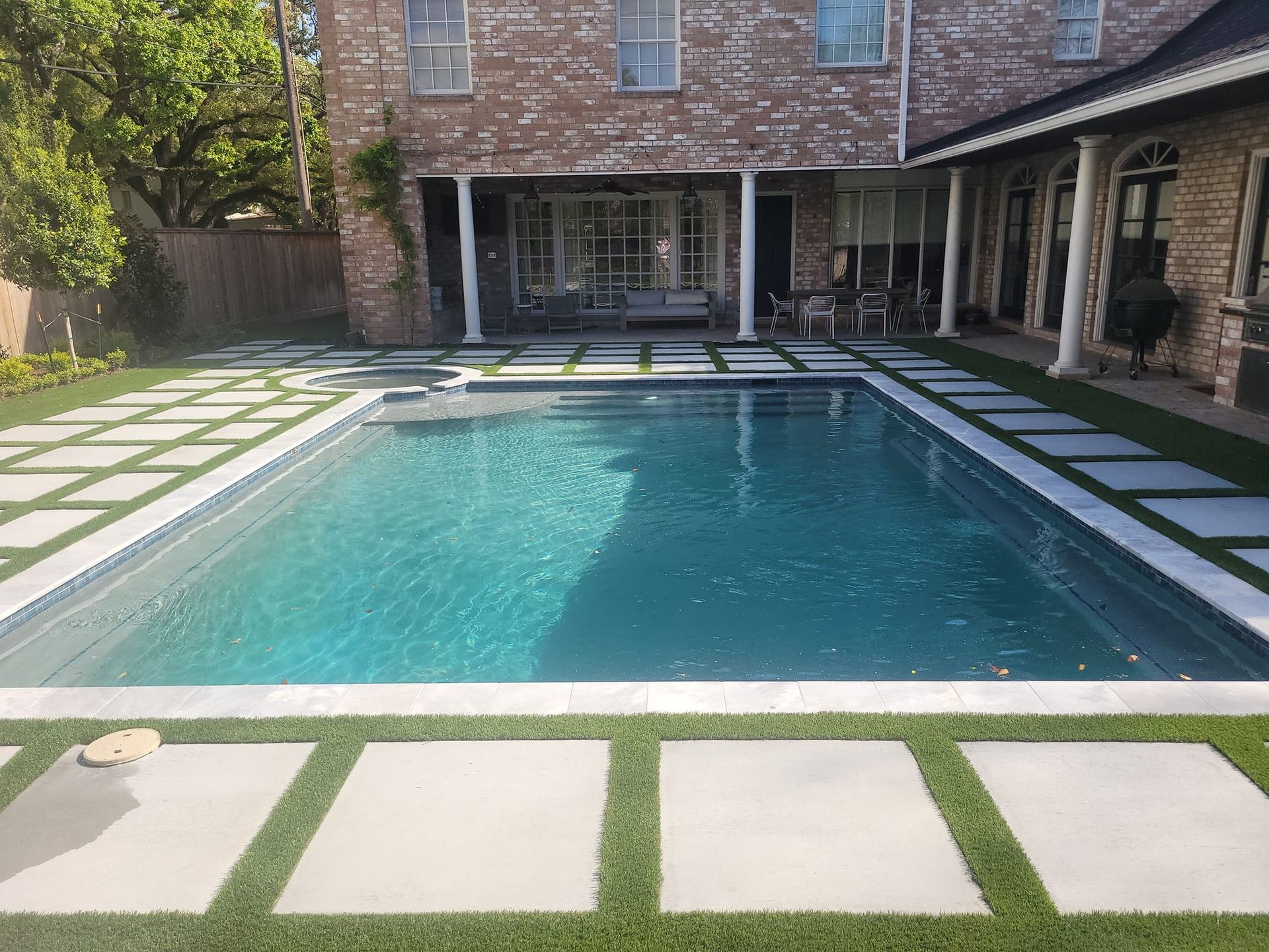 Backyard pool surrounded by stone pavers beside a brick house and covered patio