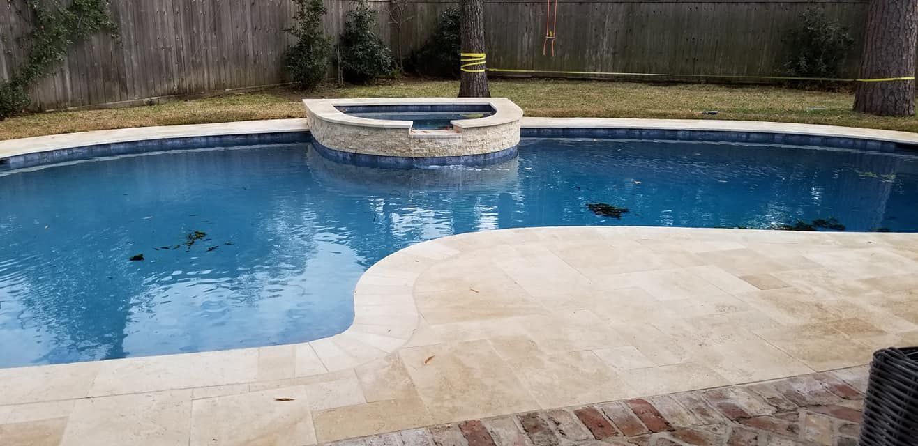 Backyard swimming pool with blue water, beige patio, and a raised spa against a wooden fence.