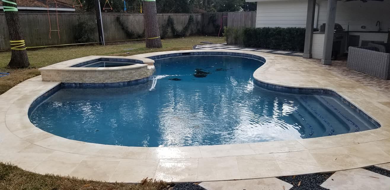 Backyard swimming pool with attached hot tub and stone deck in a fenced patio area