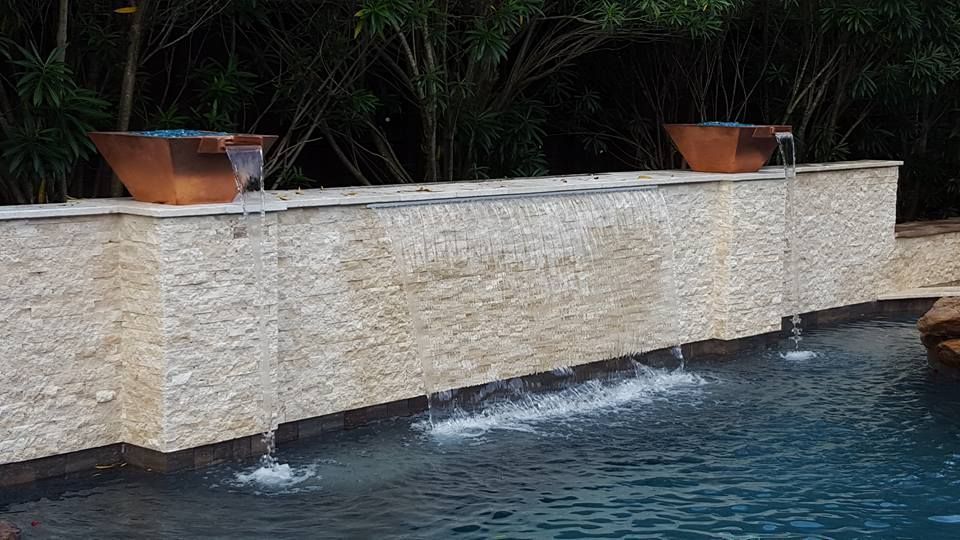 Modern stone pool wall with two orange planters and water cascading into a blue pool