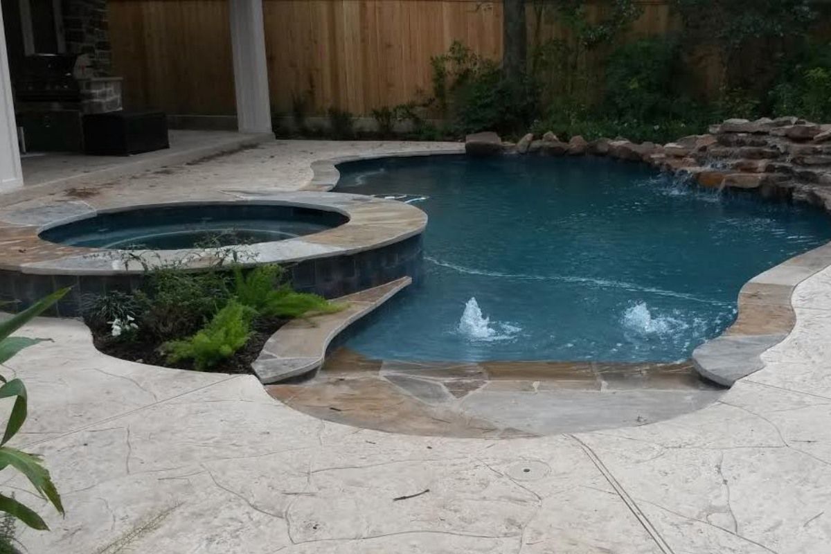 Backyard swimming pool with attached spa, stone coping, and surrounding patio at dusk