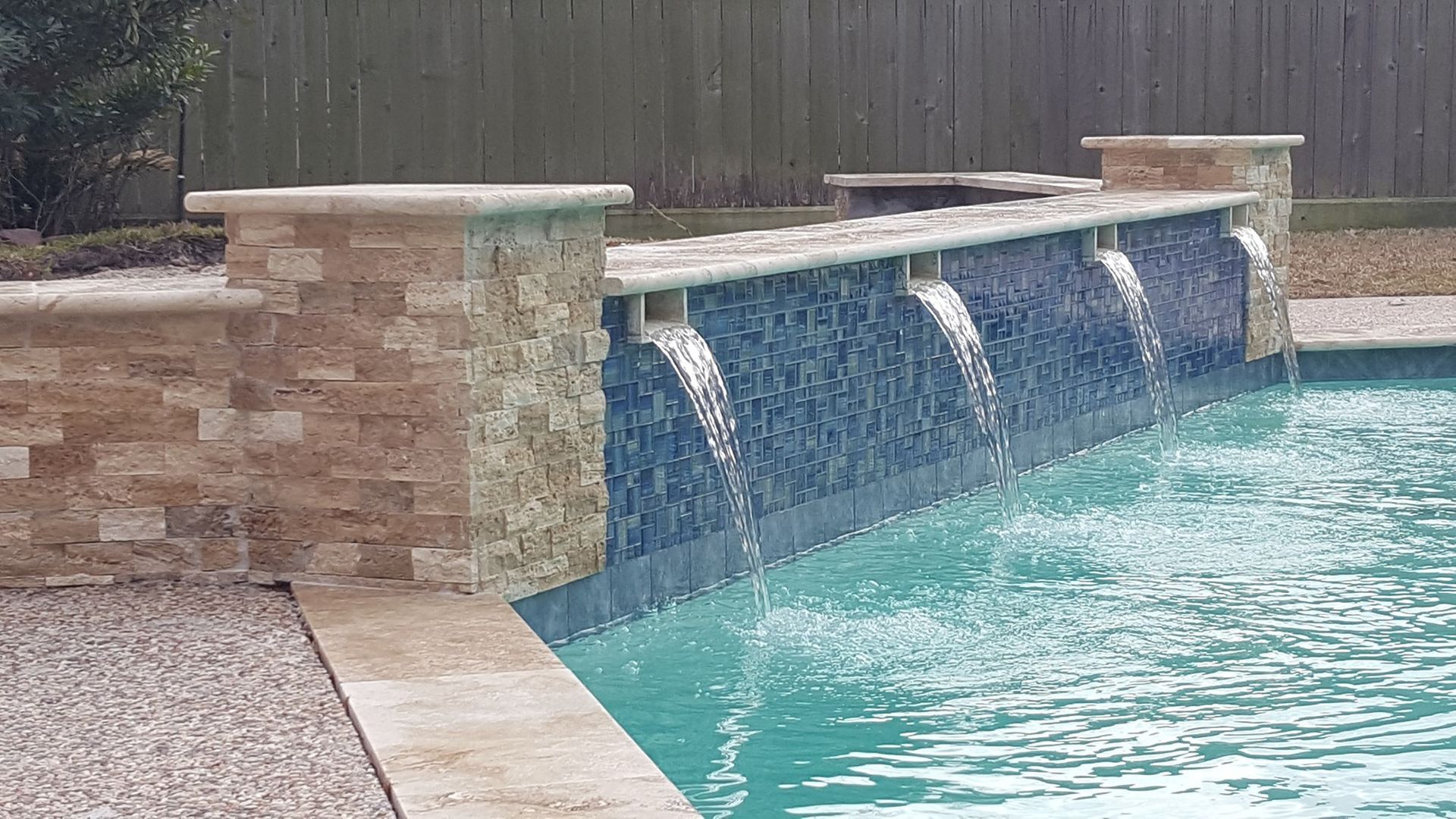 Stone waterfall feature spilling into a swimming pool in a backyard.