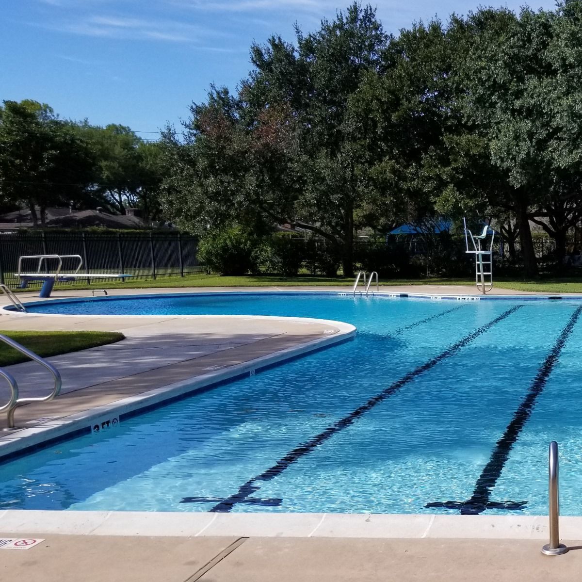 Outdoor swimming pool with blue lanes, a diving board, and trees in the background