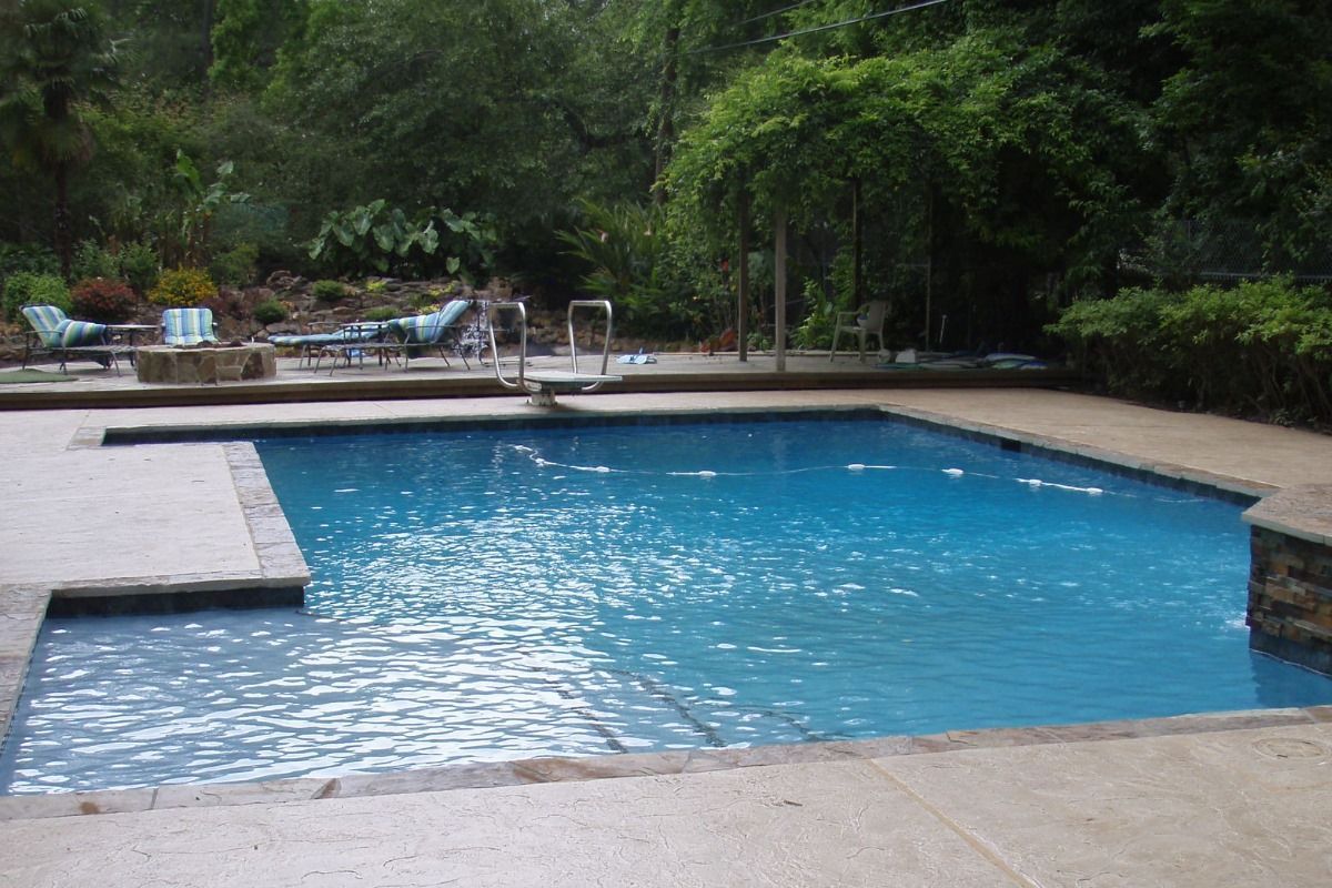 Outdoor swimming pool surrounded by concrete deck and lush green trees