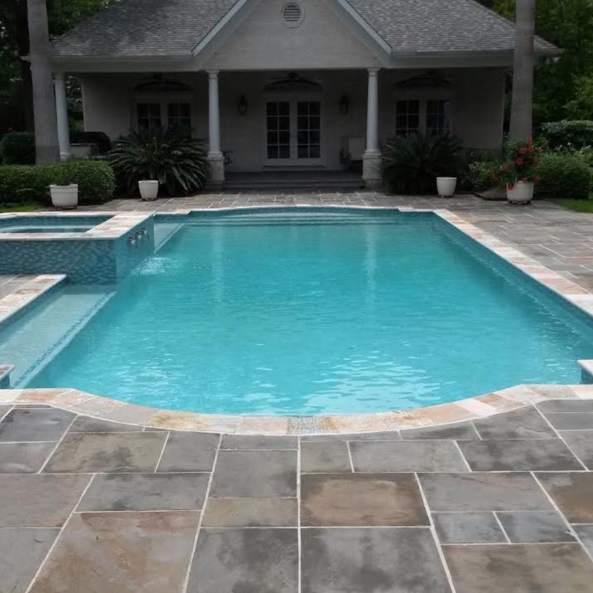 Backyard swimming pool with turquoise water and stone patio in front of a house