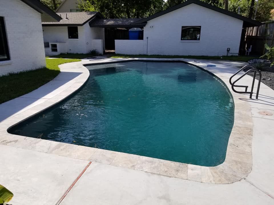 Curved backyard swimming pool with blue water, white concrete deck, and a metal handrail